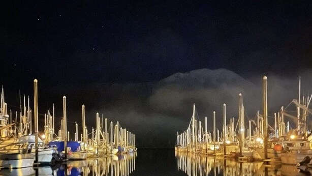 Una marina de nit amb vaixells amarrats i els seus reflexos sobre aigua tranquil·la.
