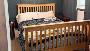 Un dormitori amb un llit de fusta, una tauleta de nit, una taula petita, una làmpada de cristall i una finestra amb cortines.