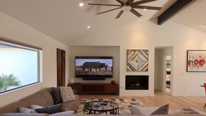 Un soggiorno moderno con una grande TV a schermo piatto, un ventilatore a soffitto e un camino.