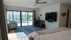 Camera d'albergo con un letto, una scrivania con una sedia, una TV e vista su una piscina.
