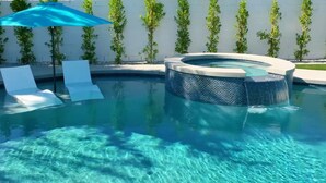 Una piscina con idromassaggio, lettini e un ombrellone blu.