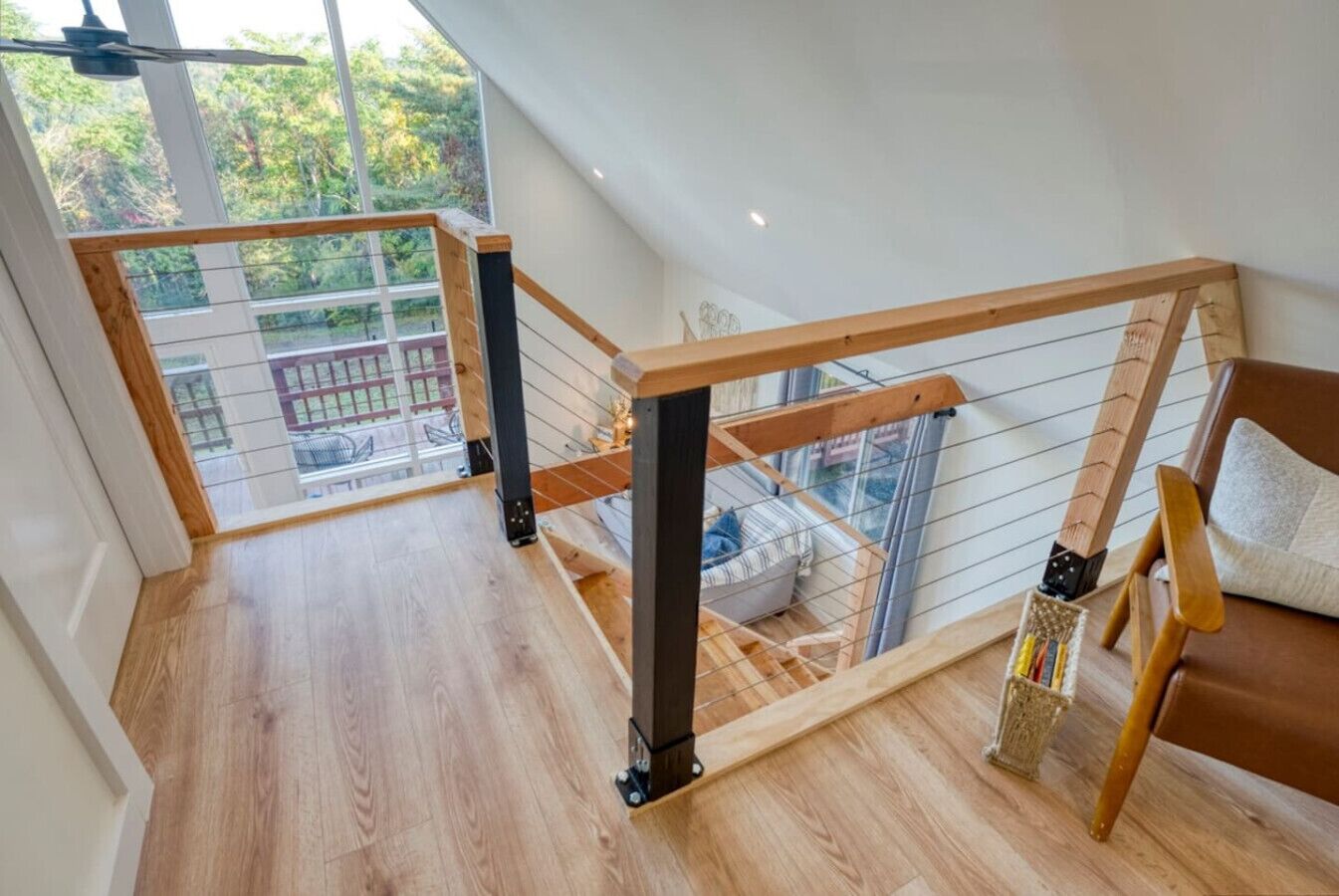 A spacious loft bedroom with a wooden floor, a wooden staircase, a large window, and a view of the outdoors.