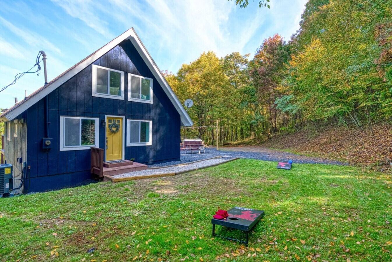 A blue house with a sloped roof, a front porch, and a yard with a trampoline and a picnic table.