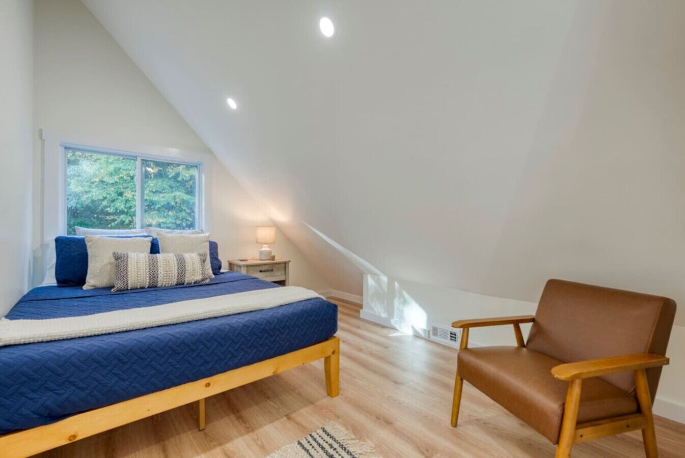 A bedroom with a bed, a chair, a nightstand, and a window.