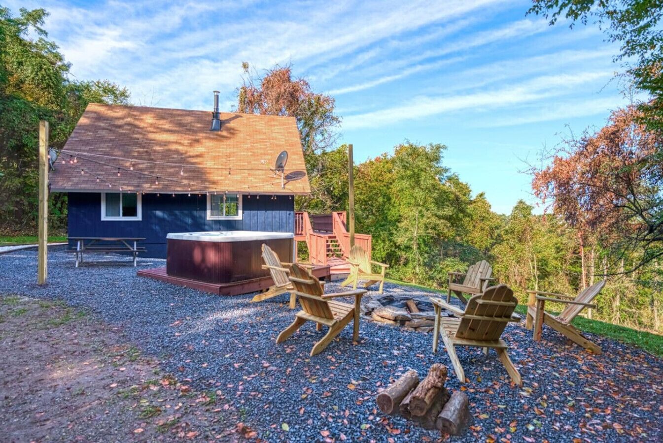 A cabin with a hot tub, wooden chairs, and a fire pit.