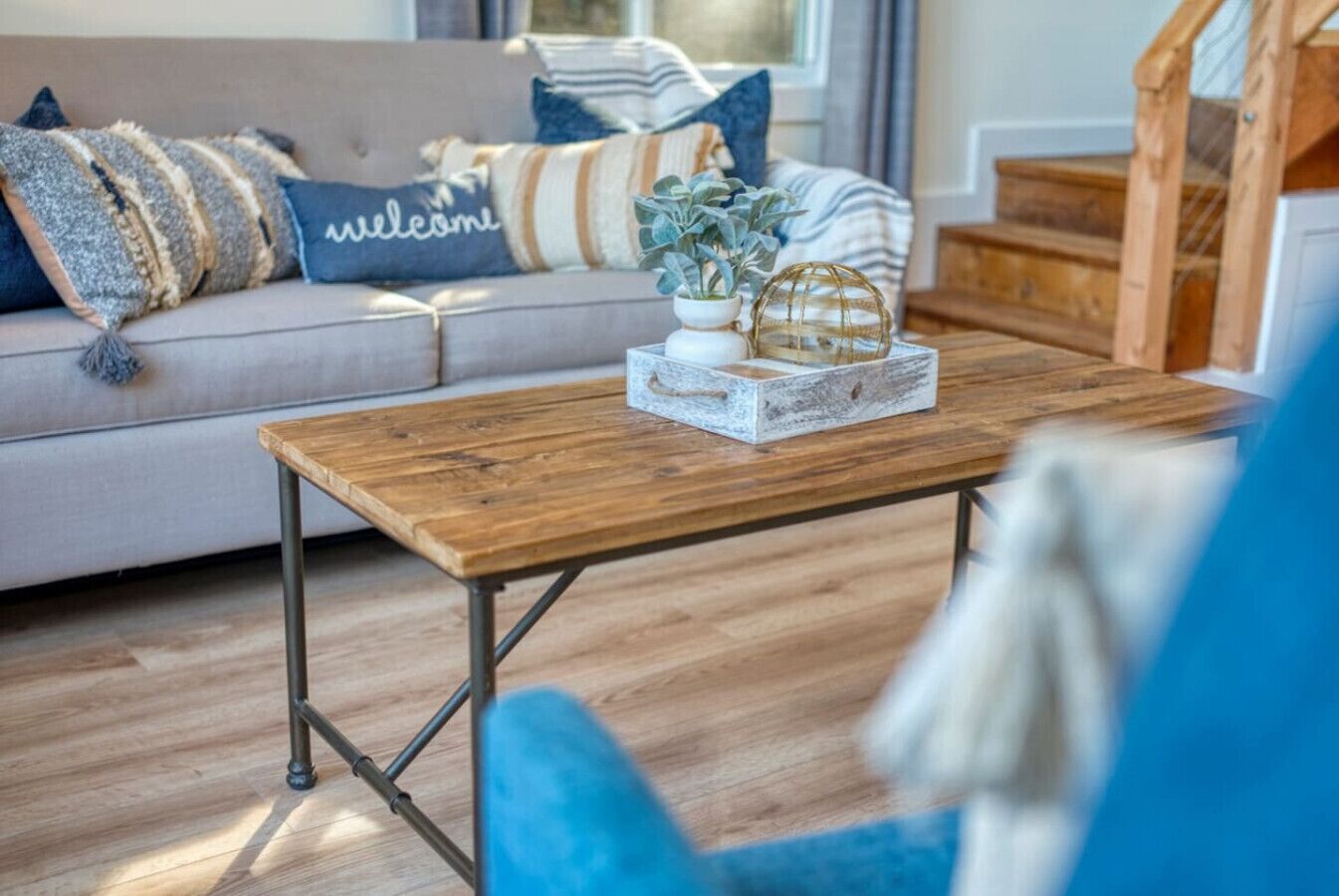 Una sala acogedora con una mesa de centro de madera, un sofá con cojines a rayas y una silla azul.
