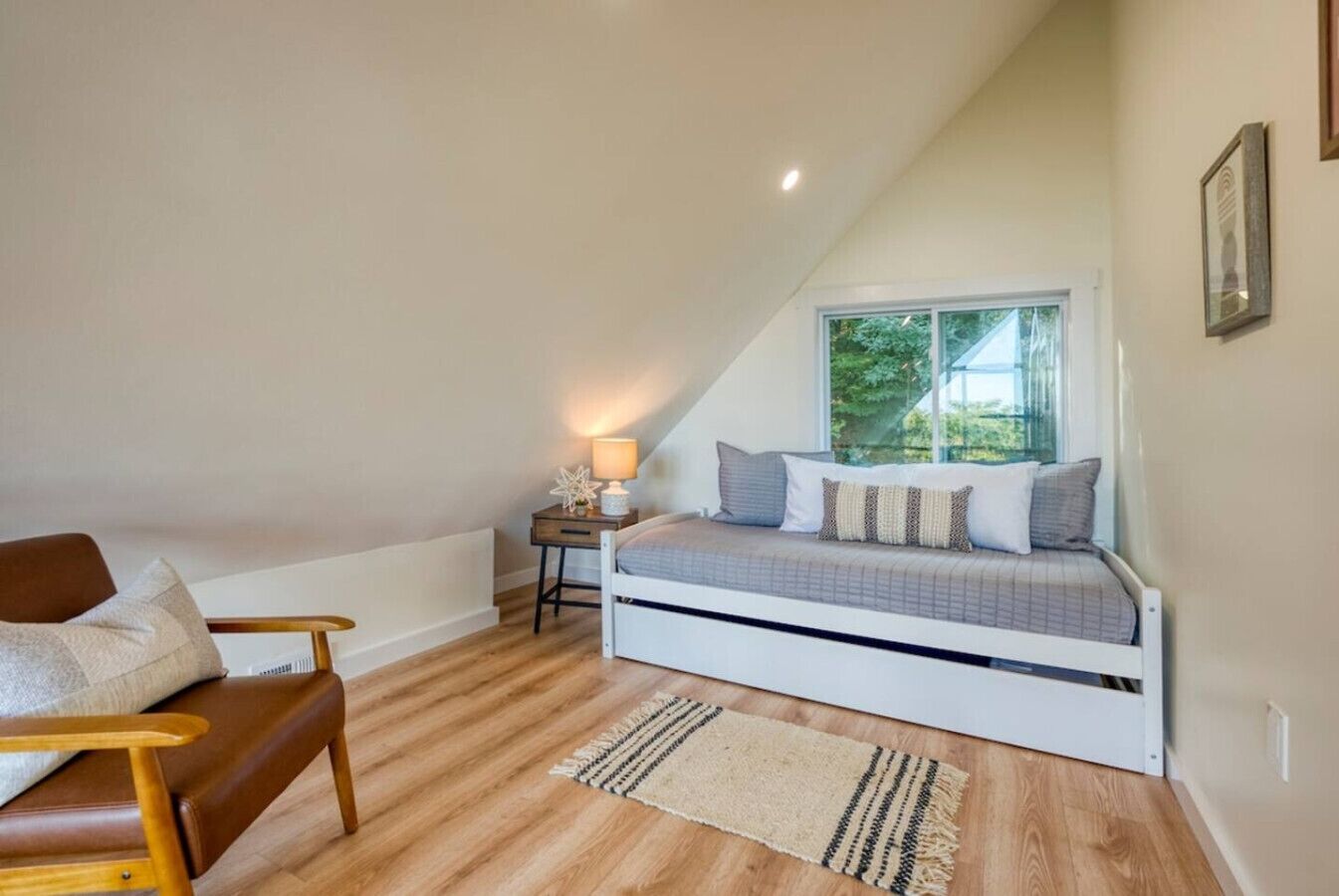 A bedroom with a sloped ceiling, a bed with a window, a nightstand, a chair, and a rug.