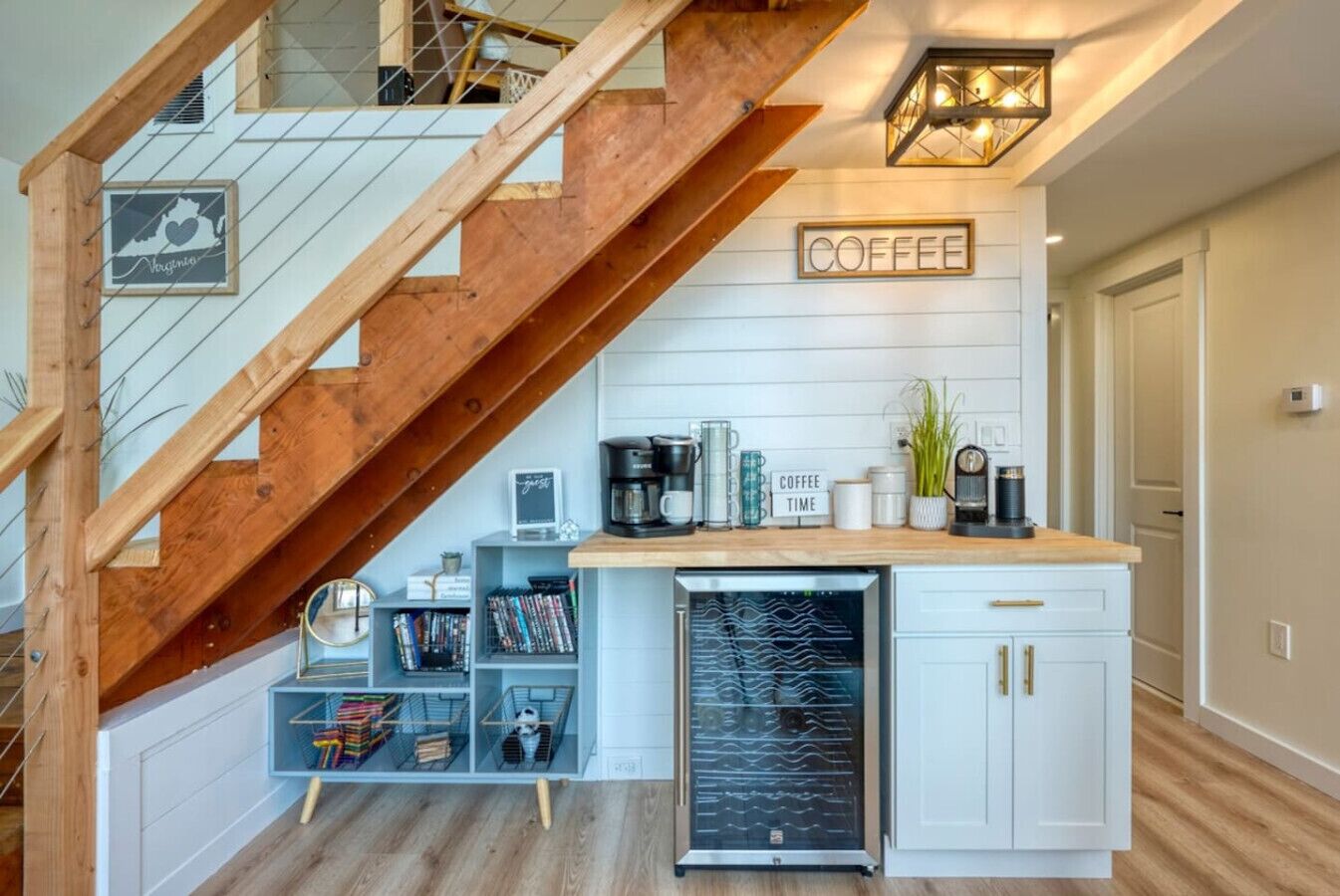 Une cuisine équipée d’un coin café, d’un escalier en bois et d’une pancarte indiquant « PAUSE CAFÉ ».