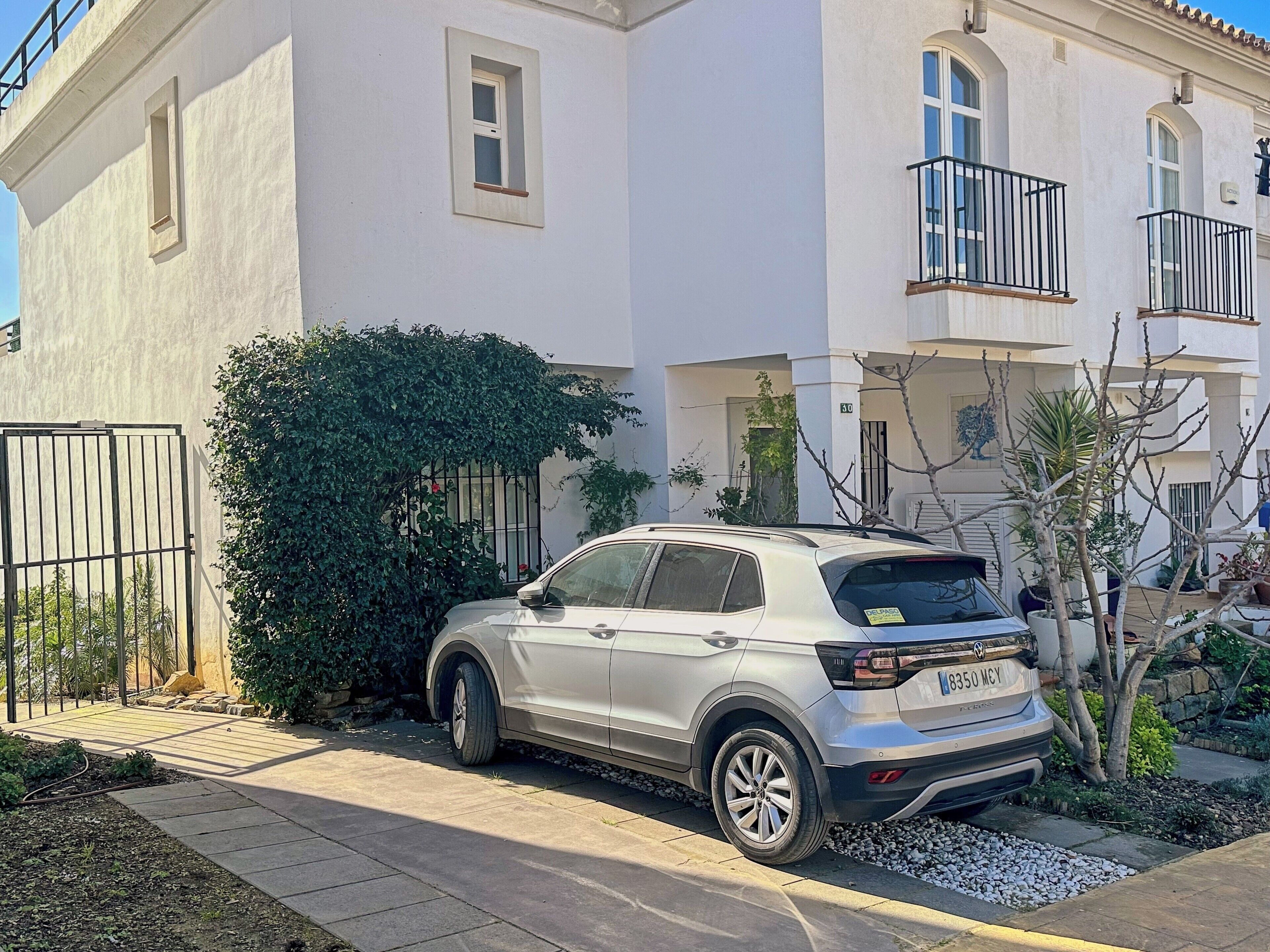 Un SUV plateado estacionado frente a un edificio blanco con balcones y una entrada con portón.