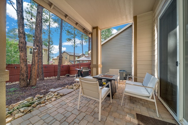 Enjoy outdoor dining or relaxation in this patio area with a table and chairs, surrounded by trees and a wooden fence.