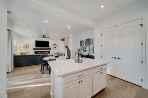 Kitchen features a central island with stove and flat-screen TV above, surrounded by white cabinetry and recessed lighting.