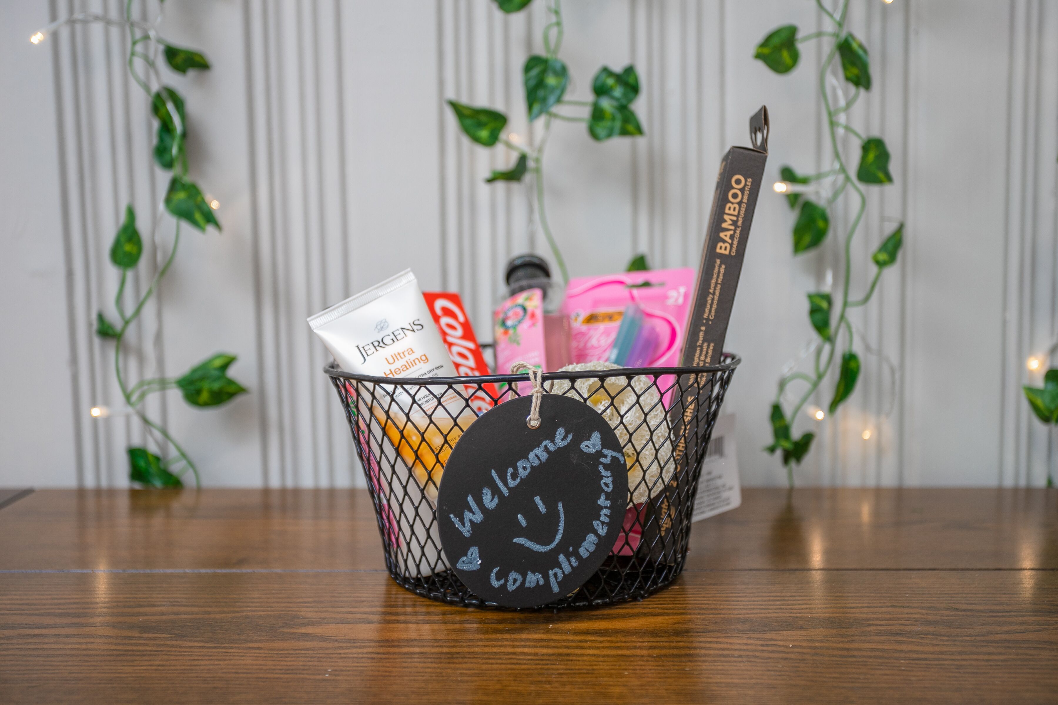 A basket with a 'Welcome & Complimentary' sign, containing various items like a toothbrush, toothpaste, and a bamboo toothbrush.
