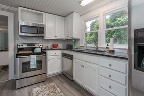 A modern kitchen with white cabinets, stainless steel appliances, and a large window providing natural light.