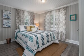 A bedroom with a large bed, a bedside table with a lamp, and a window with curtains.