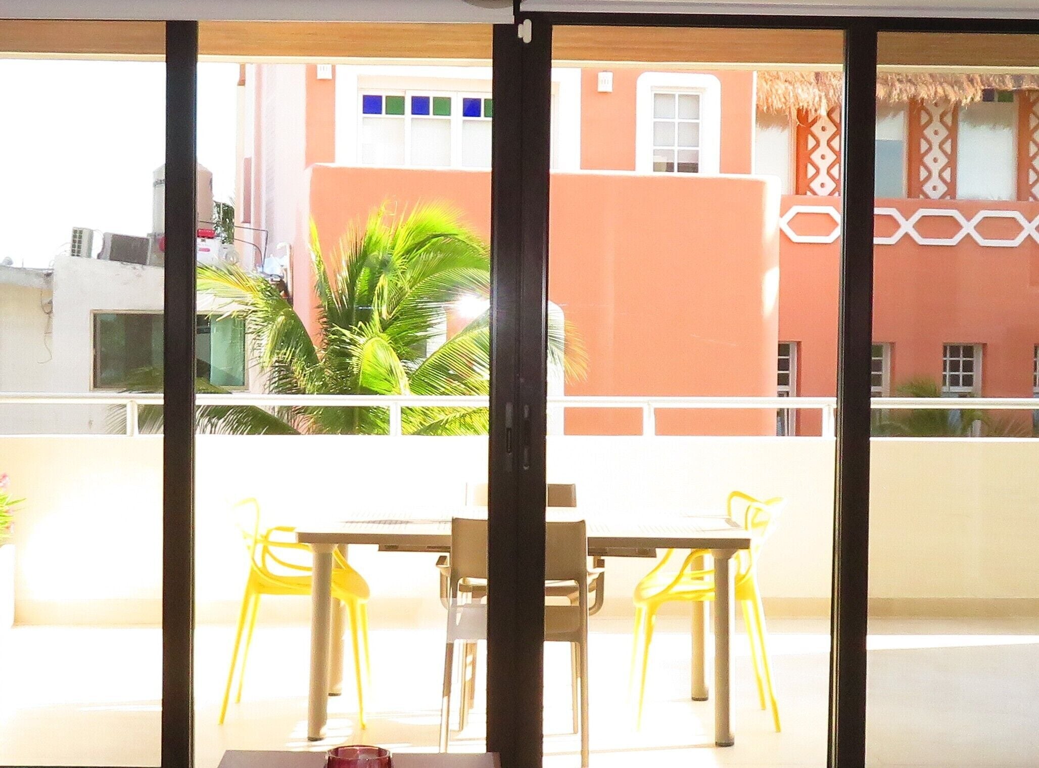 Un balcon avec des chaises jaunes et une table, donnant sur un bâtiment dont la façade est ornée de motifs et qui est surmonté d’un toit de chaume.