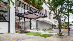 A modern building with a covered entrance, glass windows, and a landscaped area with small trees and shrubs. - Takh308 (Cancun)