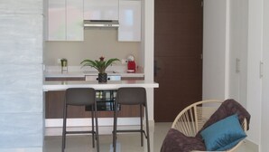 Una cocina moderna con armarios blancos, una campana extractora de acero inoxidable y una pequeña isla con dos taburetes de bar. Hay una planta en maceta en la isla y un electrodoméstico rojo sobre la encimera.