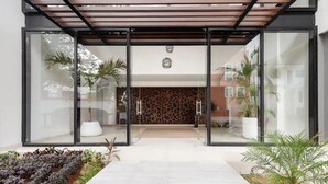 Una entrada moderna de edificio con puertas de vidrio, un muro con diseño y plantas en macetas.