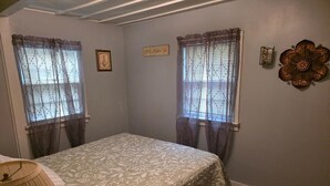 Ein Schlafzimmer mit zwei Fenstern, einem Bett mit Blumendekoration, einer Wanduhr und einem Wanddekor.
