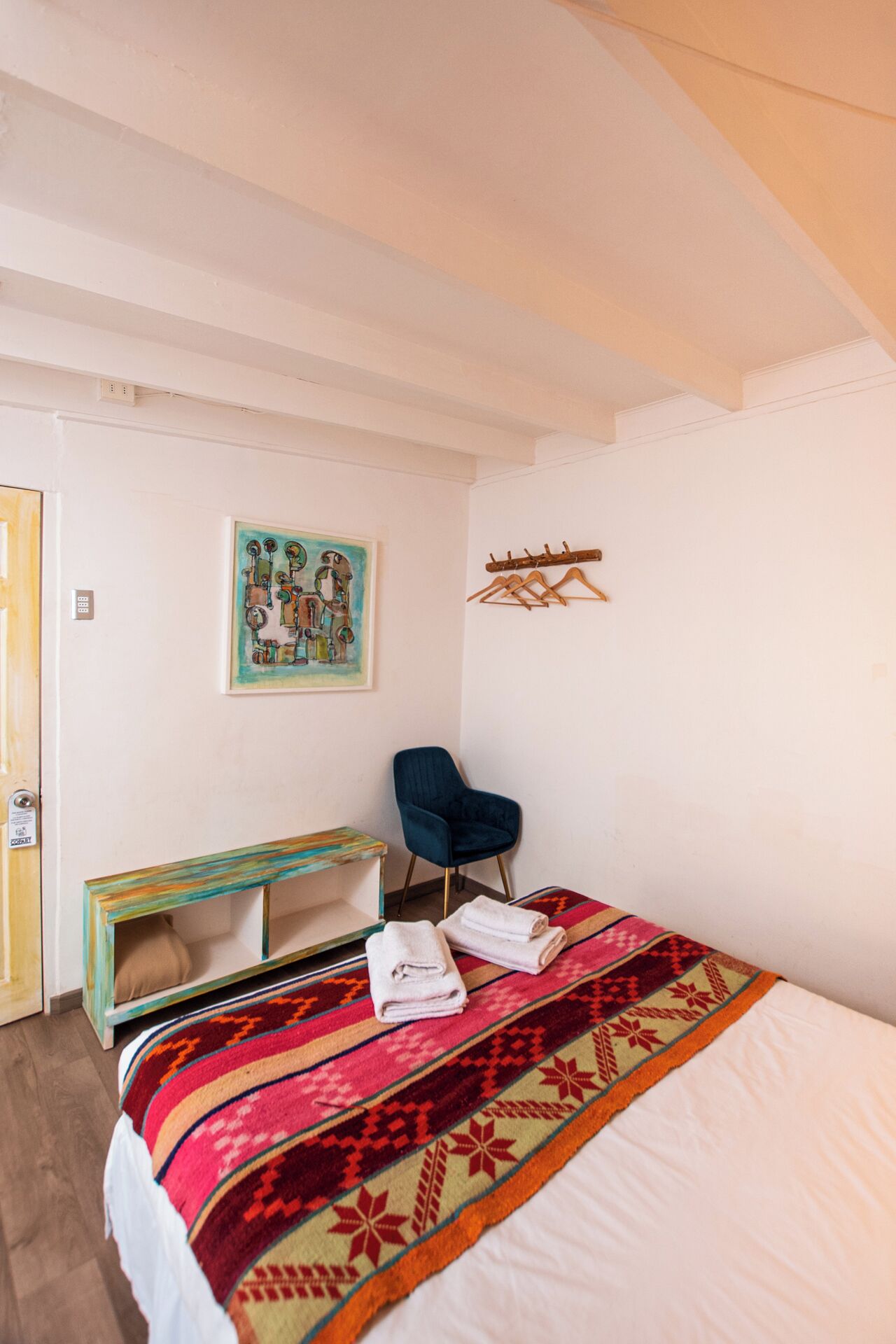 Ein Schlafzimmer mit einem Bett, einem blauen Sessel, einer farbenfrohen Bank und einem Bild an der Wand.