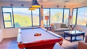A pool table in a room with large windows, a sofa, and a coffee table. - Deer Haven - Hot Tub - Game Room - Sleeps 11 (Ahwahnee)