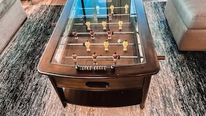 A foosball table in a room with a carpeted floor, a sofa, and a window. - Deer Haven - Hot Tub - Game Room - Sleeps 11 (Ahwahnee)