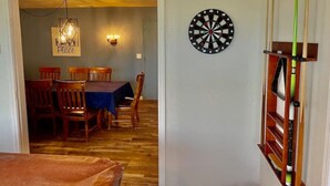 A room with a dartboard on the wall, a dining table with chairs, and a wooden floor. - Deer Haven - Hot Tub - Game Room - Sleeps 11 (Ahwahnee)