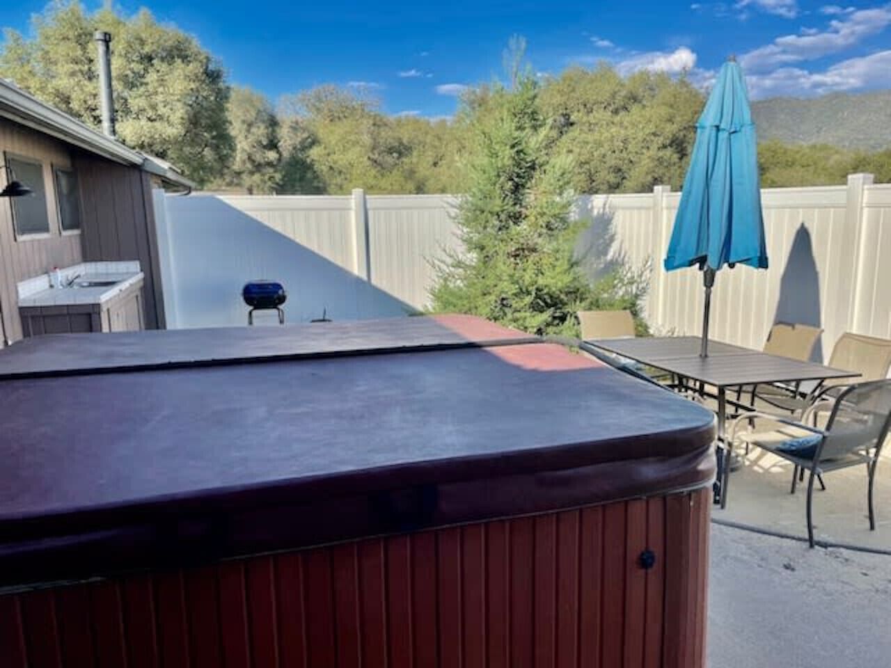 A hot tub in a backyard with a patio table and chairs, surrounded by a wooden fence and trees.