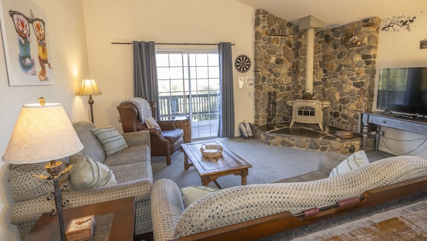 A cozy living room with a stone fireplace, a television, and a comfortable seating area with a sofa and armchairs. - Squirrel View - Hot tub/BBQ/Patio/Shuffle Board (Oakhurst)