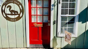 A red door with a 'Welcome' sign, a window with a striped curtain, and a 'Squirrel View Suite' sign on the wall. - Squirrel View - Hot tub/BBQ/Patio/Shuffle Board (Oakhurst)