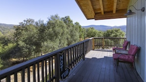A wooden deck with a "HOT TUB" sign, two red chairs, and a view of a forested landscape. - Squirrel View - Hot tub/BBQ/Patio/Shuffle Board (Oakhurst)