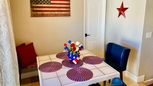Un'area pranzo con un tavolo apparecchiato per quattro persone, un vaso di fiori, una decorazione a stella rossa e una bandiera americana appesa al muro.