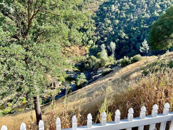 A white picket fence overlooking a hilly landscape with dense greenery and a stream.