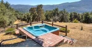 Un bain à remous installé dans un cadre naturel, entouré d’une clôture en bois, avec vue sur les montagnes.