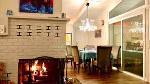 Un salon chaleureux avec une cheminée, un coin repas avec des chaises et une table, et une grande fenêtre.