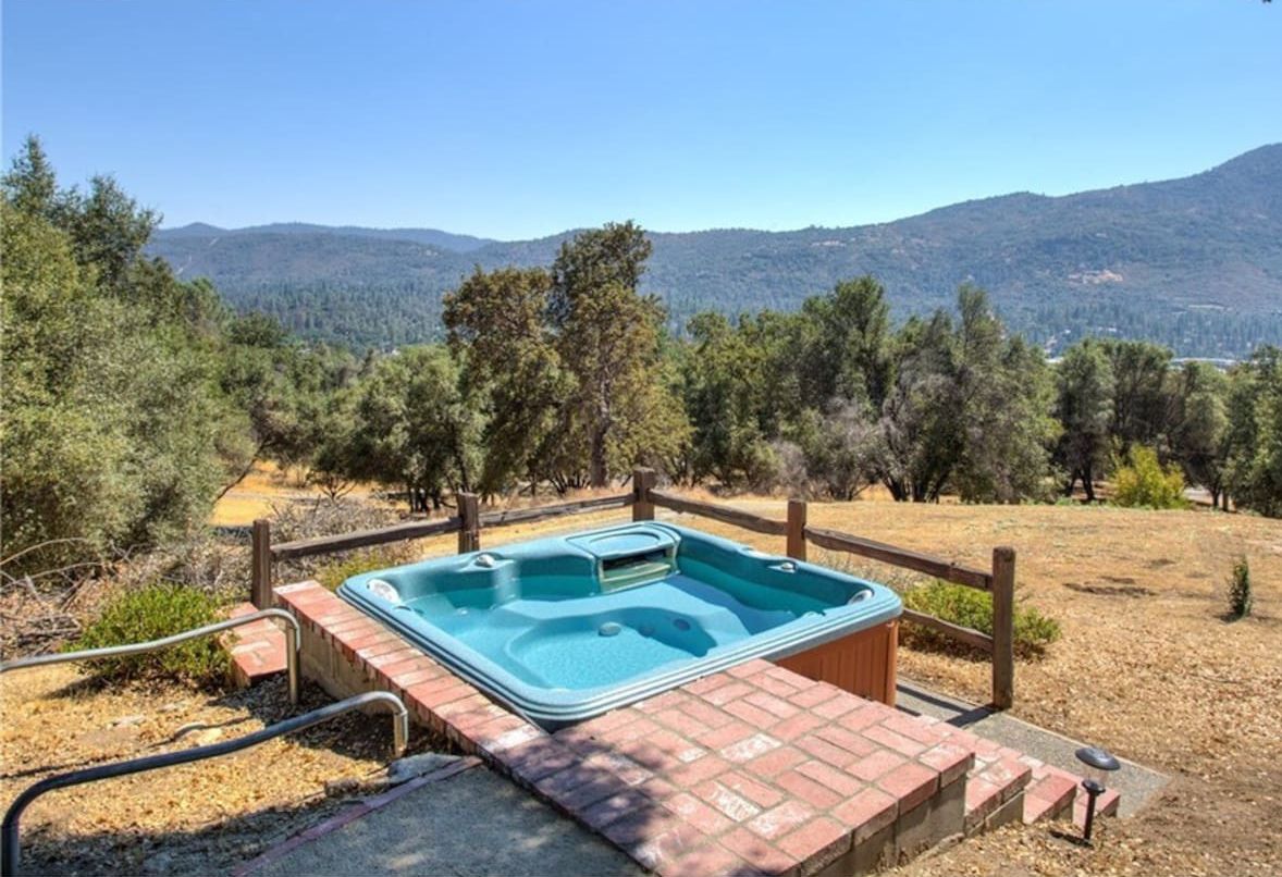 A hot tub in a natural setting with a wooden fence and a view of mountains.