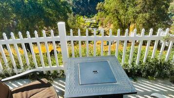 A patio with a table and chairs, a white picket fence, and a view of a river and forest.