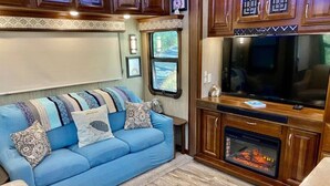 A cozy RV interior with a blue sofa, a fireplace, and wooden cabinets. - Happy Hedgehog - River Views - Hot Tub - Private (Ahwahnee)
