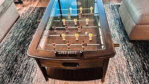 Una mesa de fútbol de mesa en una habitación con piso alfombrado, un sofá y una ventana.