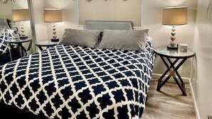 Un dormitorio con colcha estampada, dos mesitas de noche con lámparas, un espejo y una cortina con motivos florales.