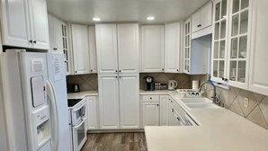 Una cocina moderna con armarios blancos, horno empotrado, refrigerador y lavaplatos.