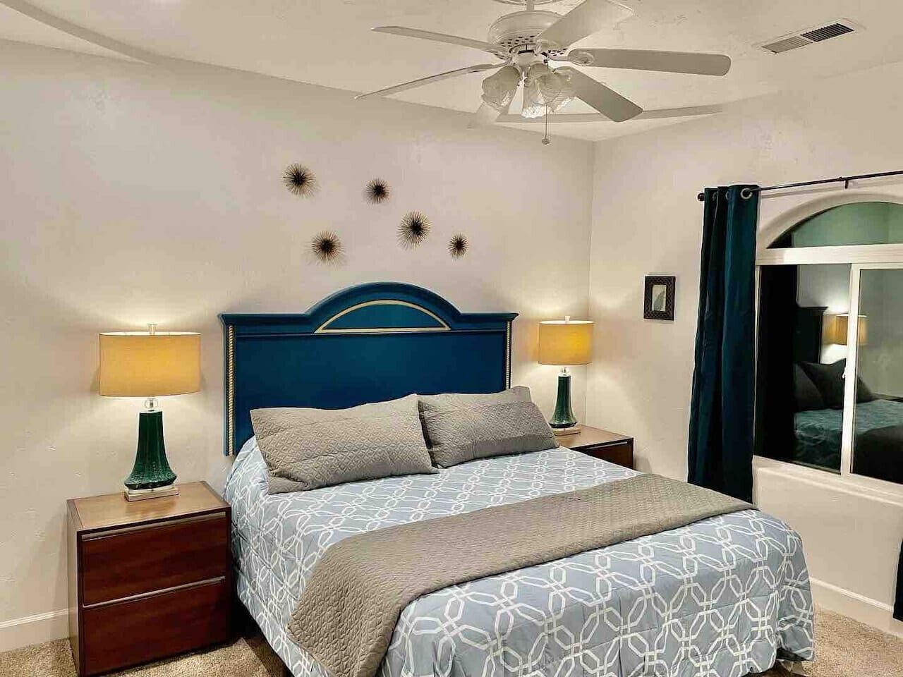 A bedroom with a bed, two bedside tables, a ceiling fan, and a window with curtains.