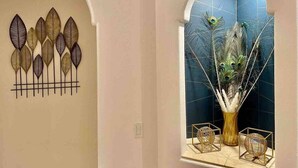 Una habitación con un adorno de plumas de pavo real en la pared y un florero con un arreglo de plumas de pavo real.