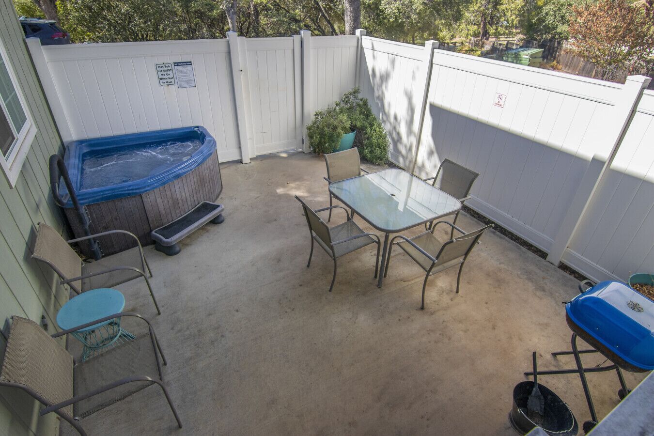 A backyard with a hot tub, a table with chairs, and a wheelbarrow.