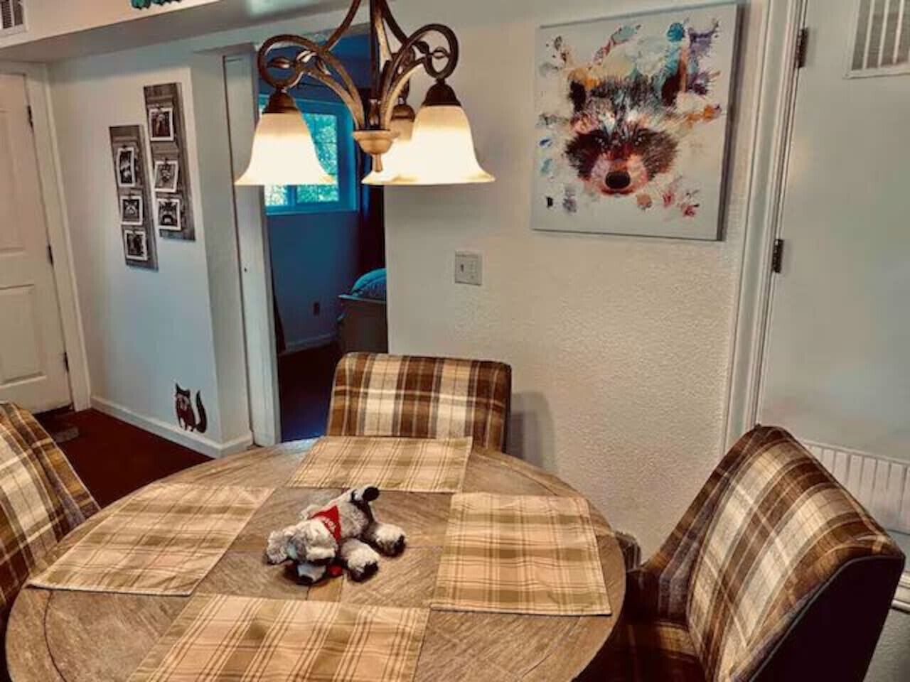 A dining area with a round table, plaid chairs, a chandelier, and a framed abstract painting.