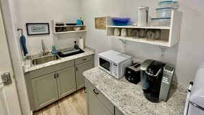 Cocina compacta con lavamanos, microondas, cafetera y estantes con utensilios de cocina.