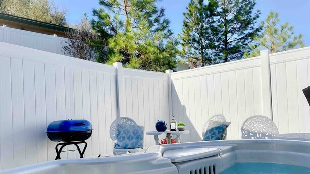 Un patio trasero con un jacuzzi, una parrilla y dos sillones estampados.