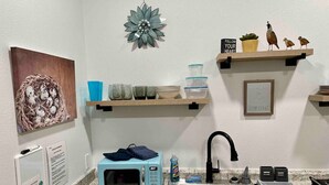 Een keuken met een magnetron, spoelbak en verschillende keukenbenodigdheden op planken.