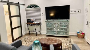 Een woonkamer met een grote flatscreen televisie, een schuifdeur in boerderijstijl, een dressoir in vintage stijl en een kamerbreed tapijt met een patroon.