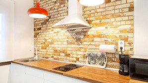 Una cocina con salpicadero de ladrillo, encimera de madera, pileta de acero inoxidable, lámparas colgantes rojas y una cafetera.